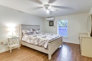 Ein Schlafzimmer mit Bett, Nachttisch mit Lampe, Deckenventilator, Klimaanlage, Fenster mit Jalousien und einem Kleiderschrank.