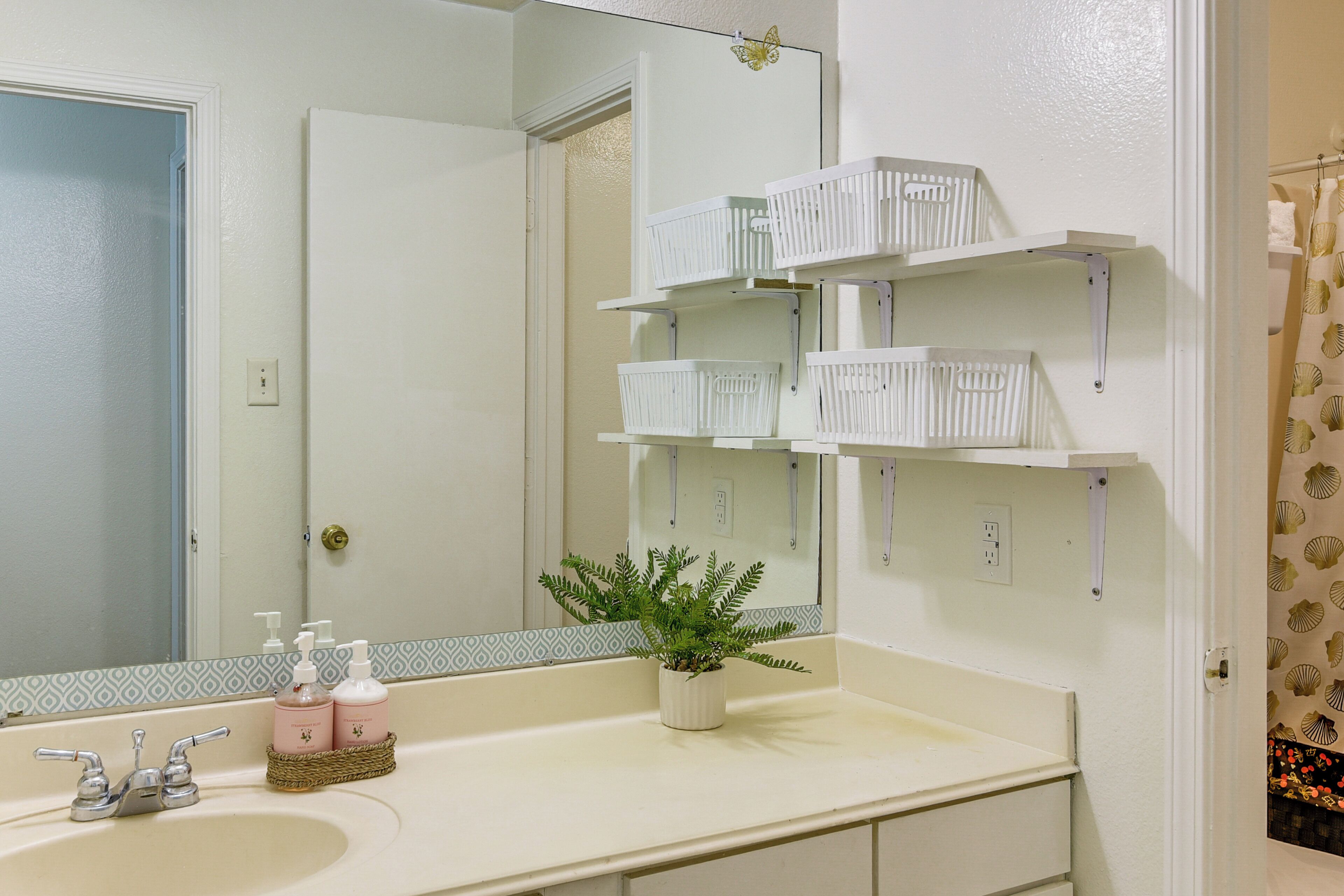 A bathroom with a white sink, a mirror, and white storage shelves above the sink.
