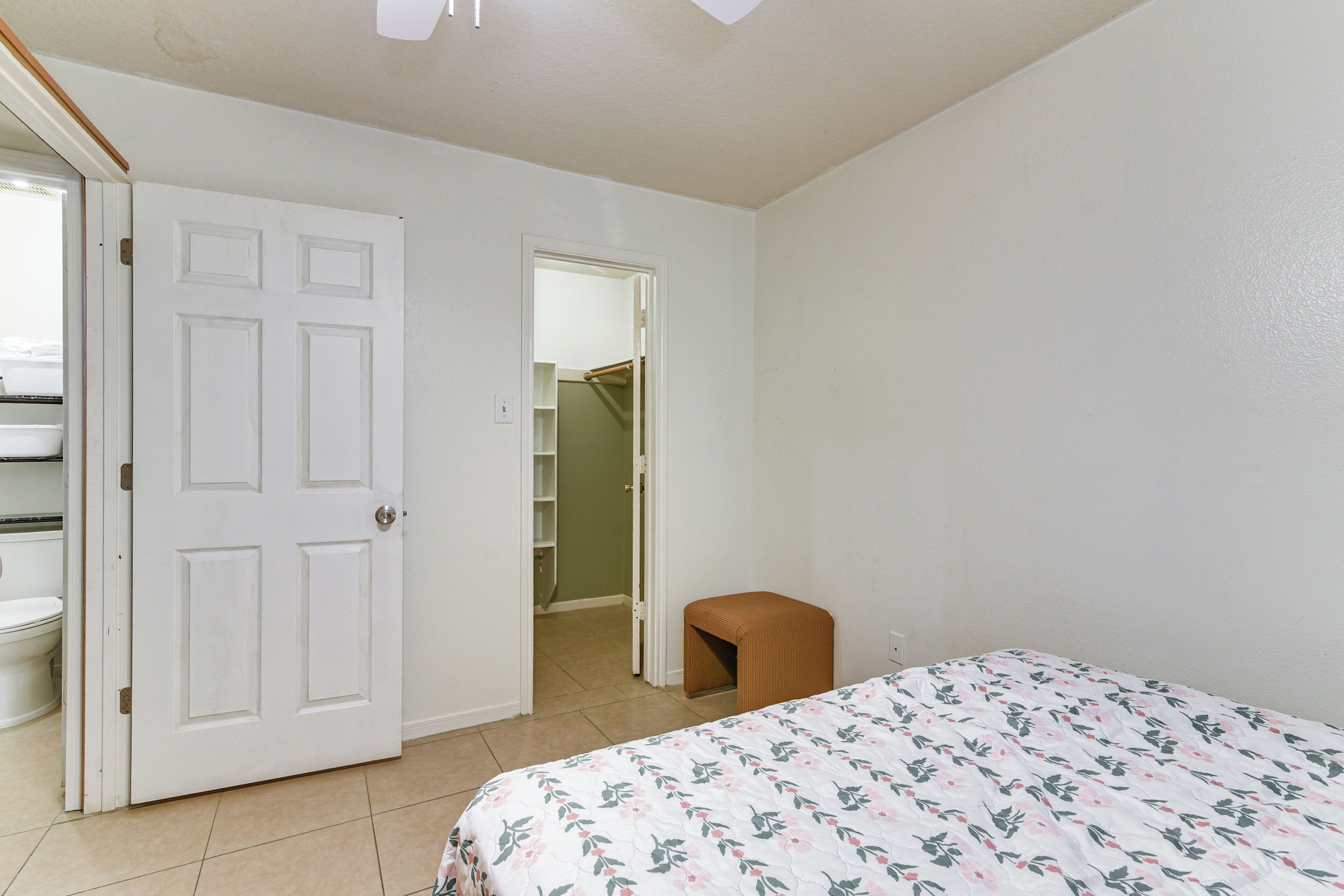 A bedroom with a bed, a door, a small stool, and a closet.