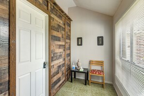 A hallway with a white door, a wooden wall, a small table with a bottle and tissues, a chair, and a window with blinds. - 2-unit Combo 10 Mi to Vintage Park & Airport! (Houston)