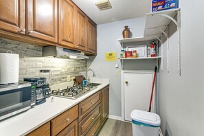 Une cuisine de taille réduite, dotée de meubles en bois, d’une cuisinière, d’un four à micro-ondes et d’une poubelle.