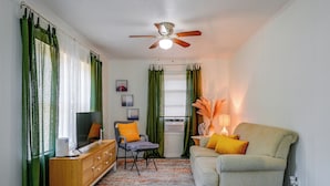 A living room with a television, a sofa, a chair, a ceiling fan, and a window with curtains. - Pet-friendly Cottage Near Beach: King Bed/fire Pit (Bonita Springs)