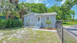 A single-story house with a front porch, surrounded by a chain-link fence, and a small yard with sparse grass and a few trees. - Pet-friendly Cottage Near Beach: King Bed/fire Pit (Bonita Springs)