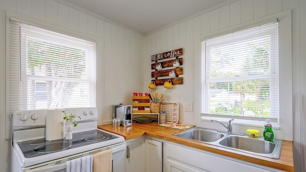 A kitchen with white cabinets, a stove, a sink, and a coffee station with mugs. - Pet-friendly Cottage Near Beach: King Bed/fire Pit (Bonita Springs)