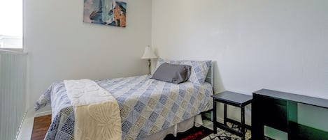 Un dormitorio con cama, un cuadro en la pared, una lámpara y un mueble para televisión.