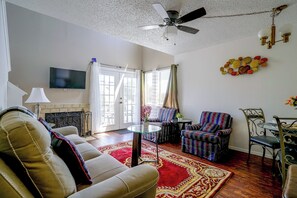 A living room with a sofa, armchairs, a TV, a ceiling fan, and a decorative wall piece. - Walk to Shops & Museums! Fort Worth Condo w/ Pool (Fort Worth)