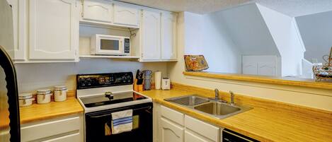 A kitchen with white cabinets, a microwave, a stove, a sink, and a wooden countertop.