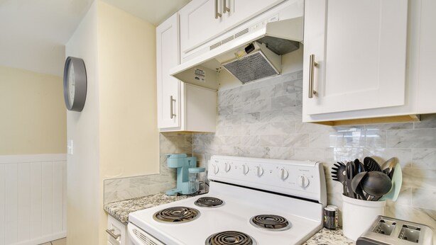 A kitchen with white cabinets, a white stove, and a coffee maker. - Unwind Poolside, Walk to Shore! Orange Beach Condo (Orange Beach)