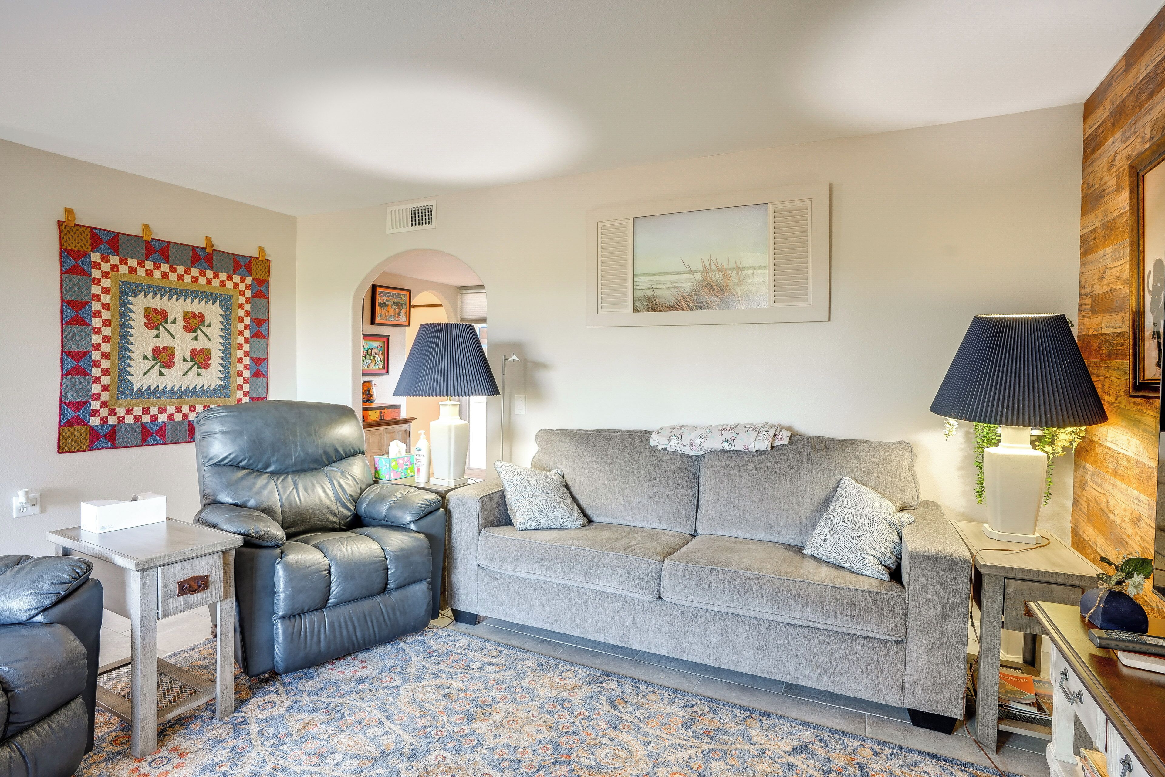 Ein Wohnzimmer mit Ledersessel, grauem Sofa, gemustertem Teppich und Wandbildern.