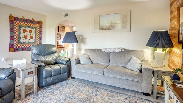 A living room with a leather chair, a grey sofa, a patterned rug, and wall art. - Steps to Golf! Extended Sun City West Getaway (Sun City West)