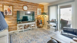 A living room with a television, a piano, a sofa, and a large window. - Steps to Golf! Extended Sun City West Getaway (Sun City West)