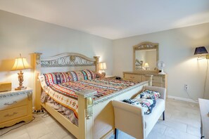 Ein Schlafzimmer mit Bett, Nachttischen, einem Schminktisch, einem Sessel, einem Spiegel und einem Wandventilator.