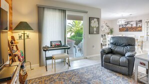 A living room with a black leather sofa, a small table, a lamp, a keyboard, and a view of the outdoors. - Steps to Golf! Extended Sun City West Getaway (Sun City West)