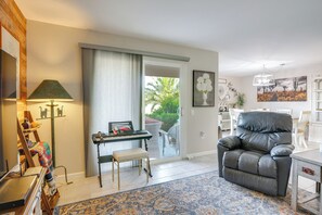Ein Wohnzimmer mit einer schwarzen Ledersofa, einem kleinen Tisch, einer Lampe, einer Tastatur und Blick ins Freie.