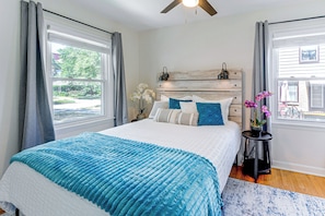 A bedroom with a bed, curtains, a nightstand, a lamp, and a view of the outside.