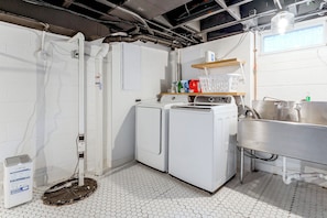 Un cuarto de lavandería con dos lavadoras, un lavabo y un estante con productos de limpieza.