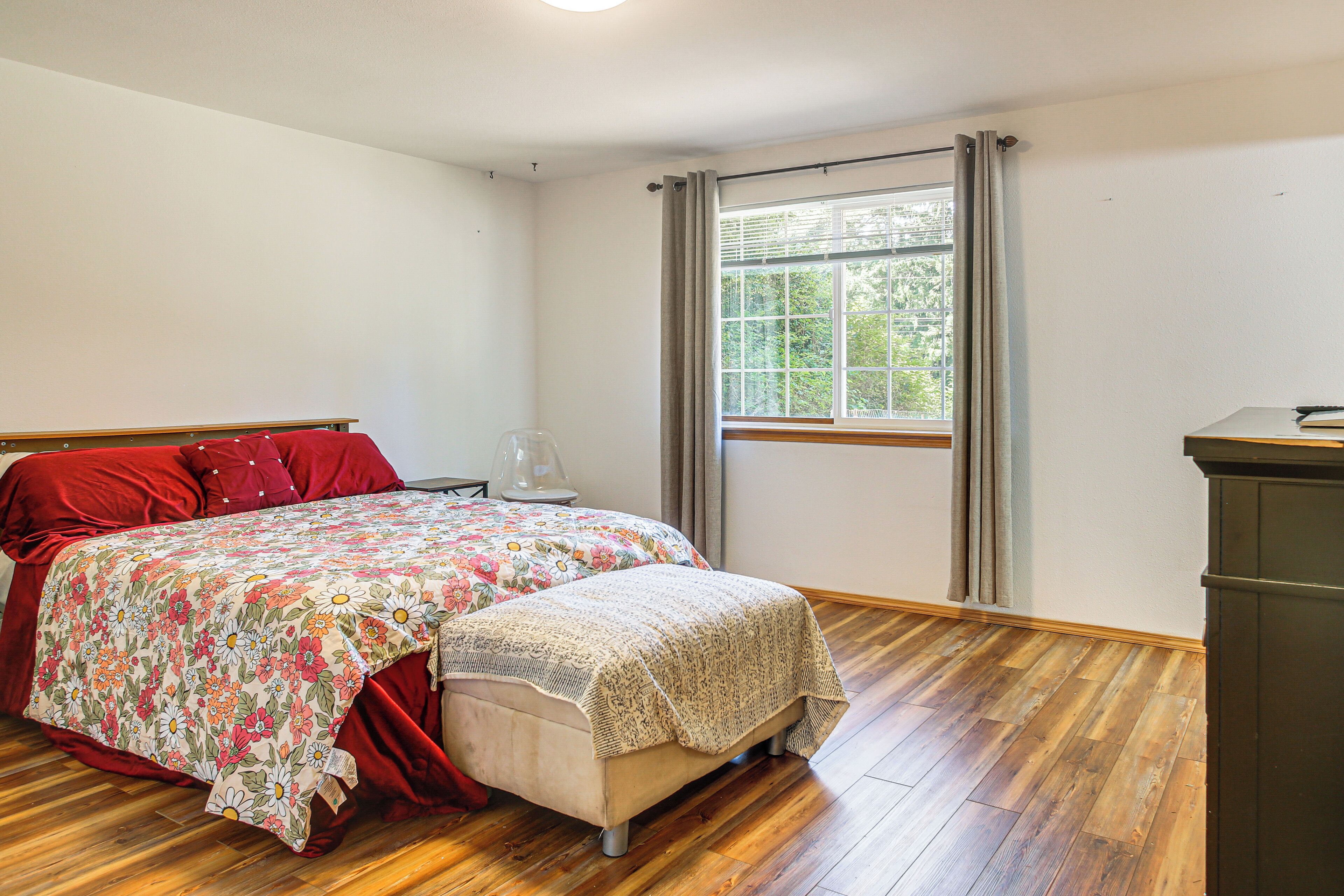A bedroom with a bed, a nightstand, a dresser, a window with curtains, and a wooden floor.