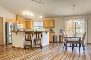 A modern kitchen with wooden cabinets, a stainless steel refrigerator, a microwave, and a dining area with a table and chairs. - Wooded Retreat 2 Mi to Kitsap Memorial State Park! (Poulsbo)