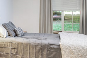 A bedroom with a bed, pillows, a window with curtains, and a view of greenery outside.