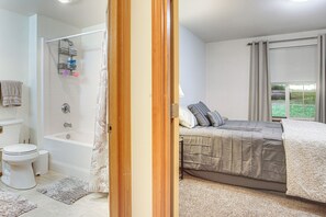 A bedroom with a bed, a window with curtains, a bathroom with a bathtub, and a toilet. - Wooded Retreat 2 Mi to Kitsap Memorial State Park! (Poulsbo)