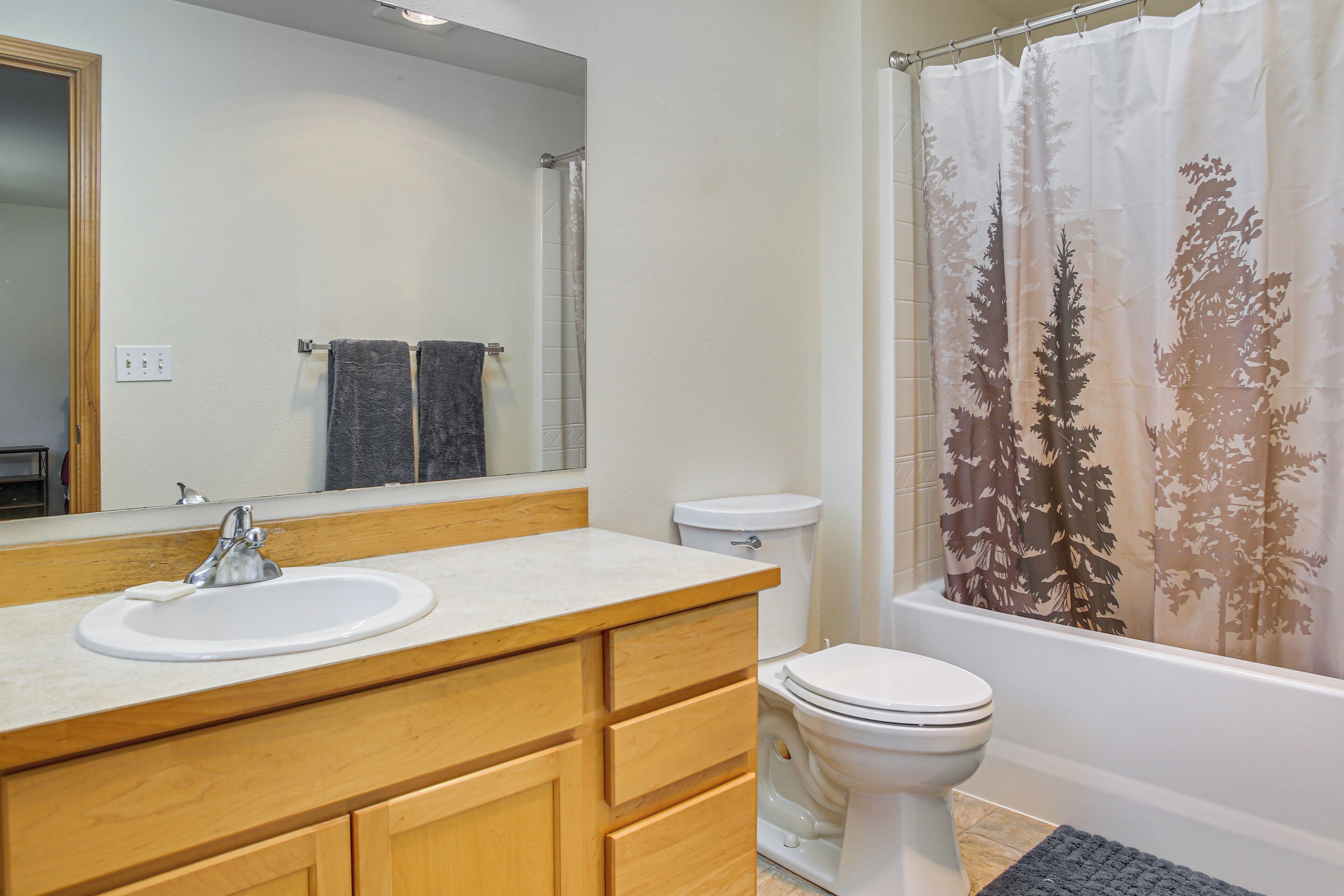 A bathroom with a white sink, wooden vanity, a mirror, a toilet, and a shower curtain with a tree pattern.