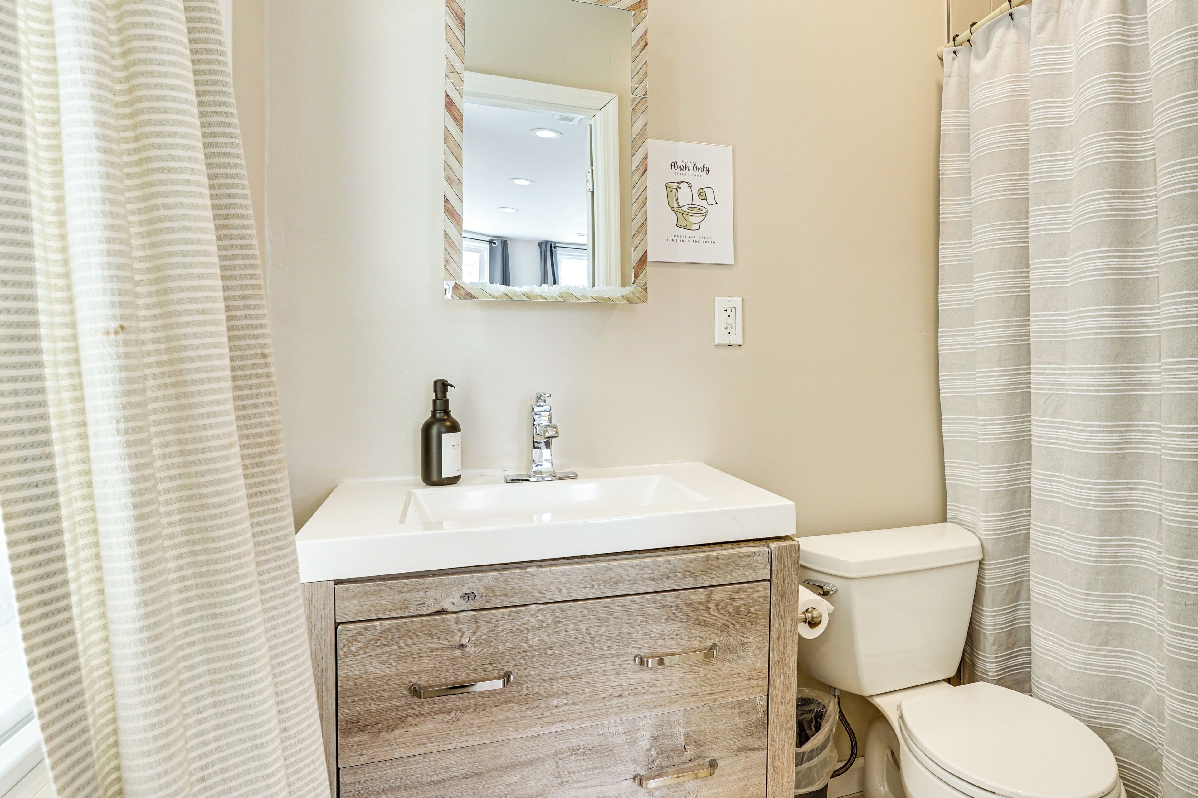 A bathroom with a white sink, a mirror, a toilet, and a wooden cabinet with drawers.