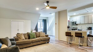 A modern living room with a sofa, a coffee table, and a rug. There is a kitchen area with a microwave, stove, and bar stools.