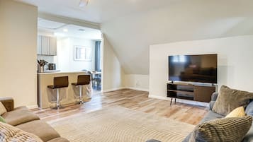 A modern living room with a flat-screen TV, a sofa, and a dining area with chairs.