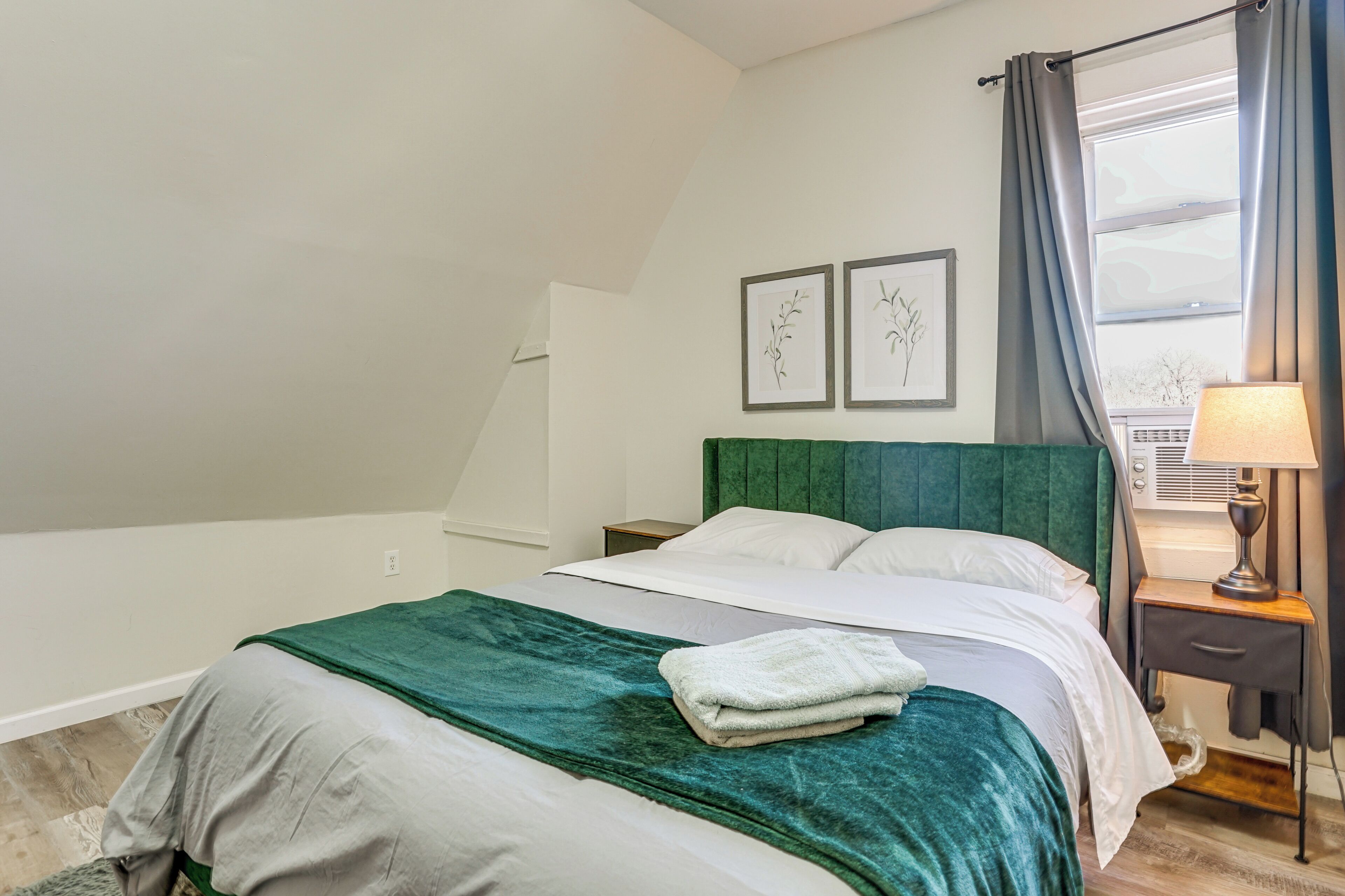 A bedroom with a bed, a nightstand, a lamp, and two framed pictures on the wall.