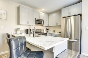 Una cocina moderna con armarios blancos, un refrigerador de acero inoxidable, un microondas integrado y una isla de encimera de mármol con asientos.
