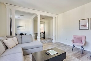 A modern living room with a sectional sofa, a coffee table, a pink armchair, and a staircase leading to another level. - Spacious Newark Duplex w/ 2 Levels & 2 Kitchens! (Newark)
