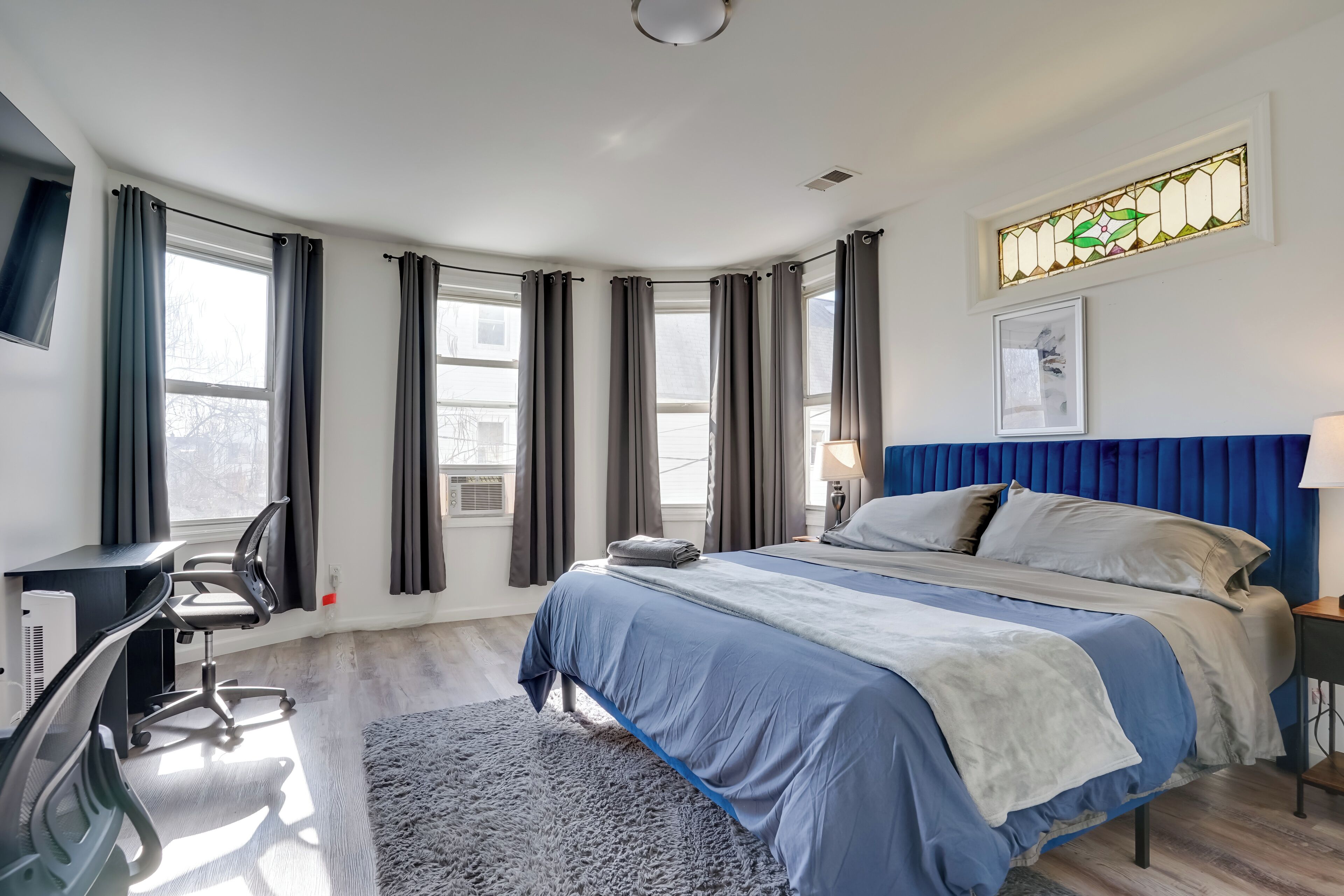Un dormitorio moderno con cama, escritorio, silla y un ventanal con cortinas.