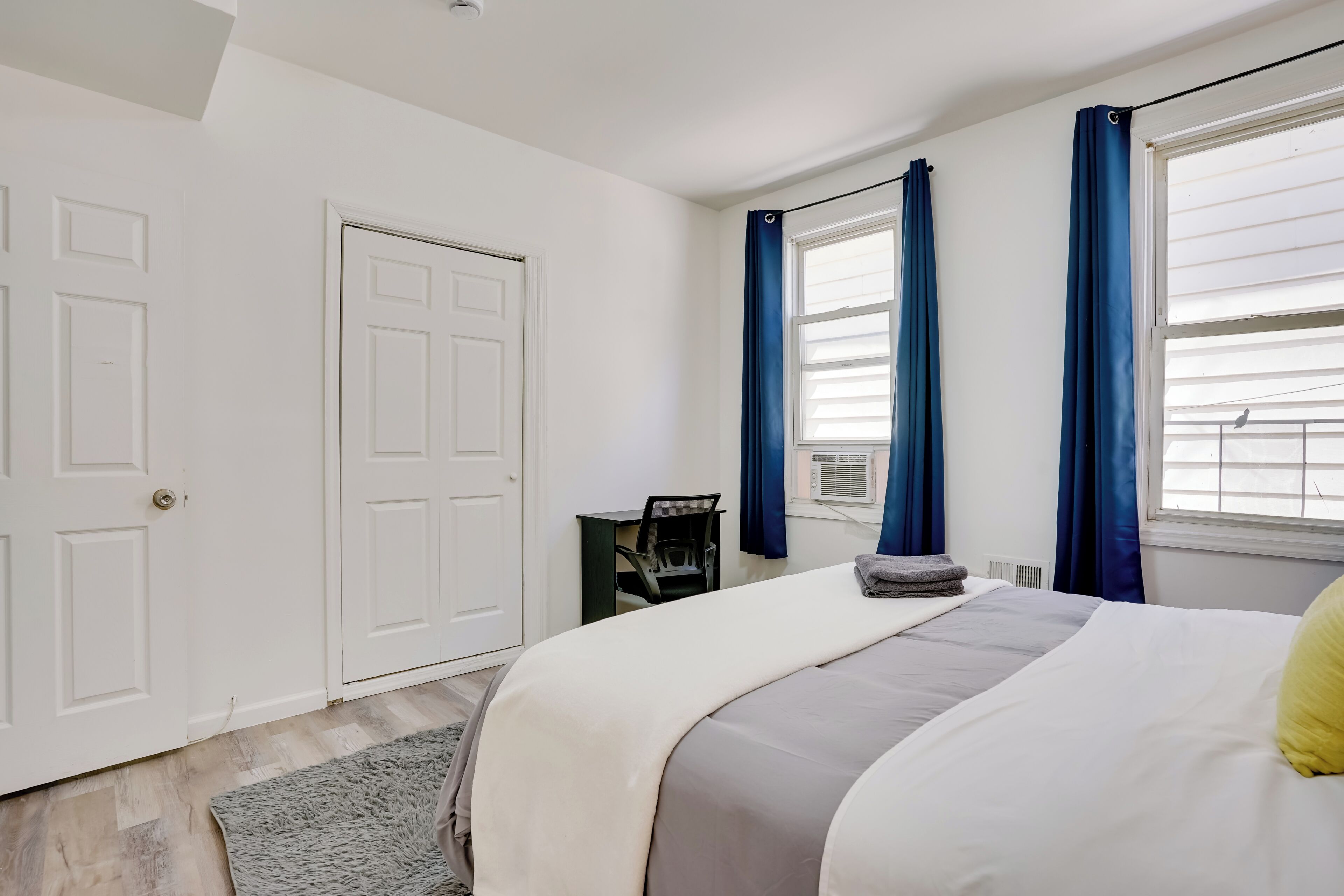 Ein Schlafzimmer mit Bett, Schreibtisch und einem fenster mit Vorhängen.