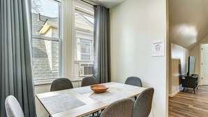 A dining area with a table, chairs, and a bowl. There is a window with curtains, an air conditioning unit, and a sign on the wall. - Spacious Newark Duplex w/ 2 Levels & 2 Kitchens! (Newark)