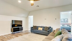 A living room with a flat-screen TV, a dark-colored sofa, a patterned rug, and a wooden ceiling fan. - Spacious Newark Duplex w/ 2 Levels & 2 Kitchens! (Newark)