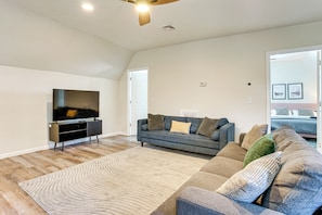 A living room with a flat-screen TV, a dark-colored sofa, a patterned rug, and a wooden ceiling fan. - Spacious Newark Duplex w/ 2 Levels & 2 Kitchens! (Newark)