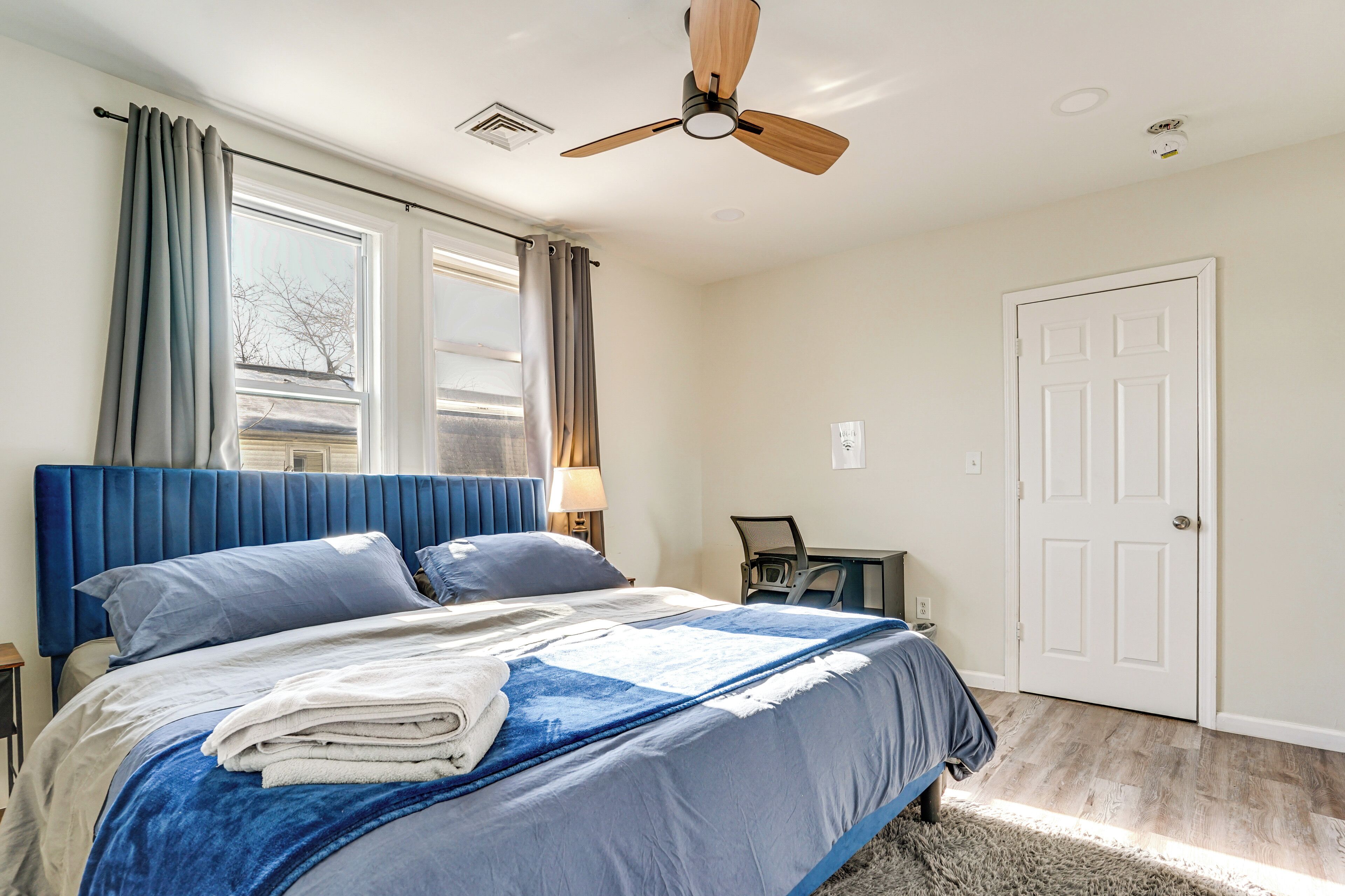 A bedroom with a bed, a desk, a chair, a ceiling fan, and a door.