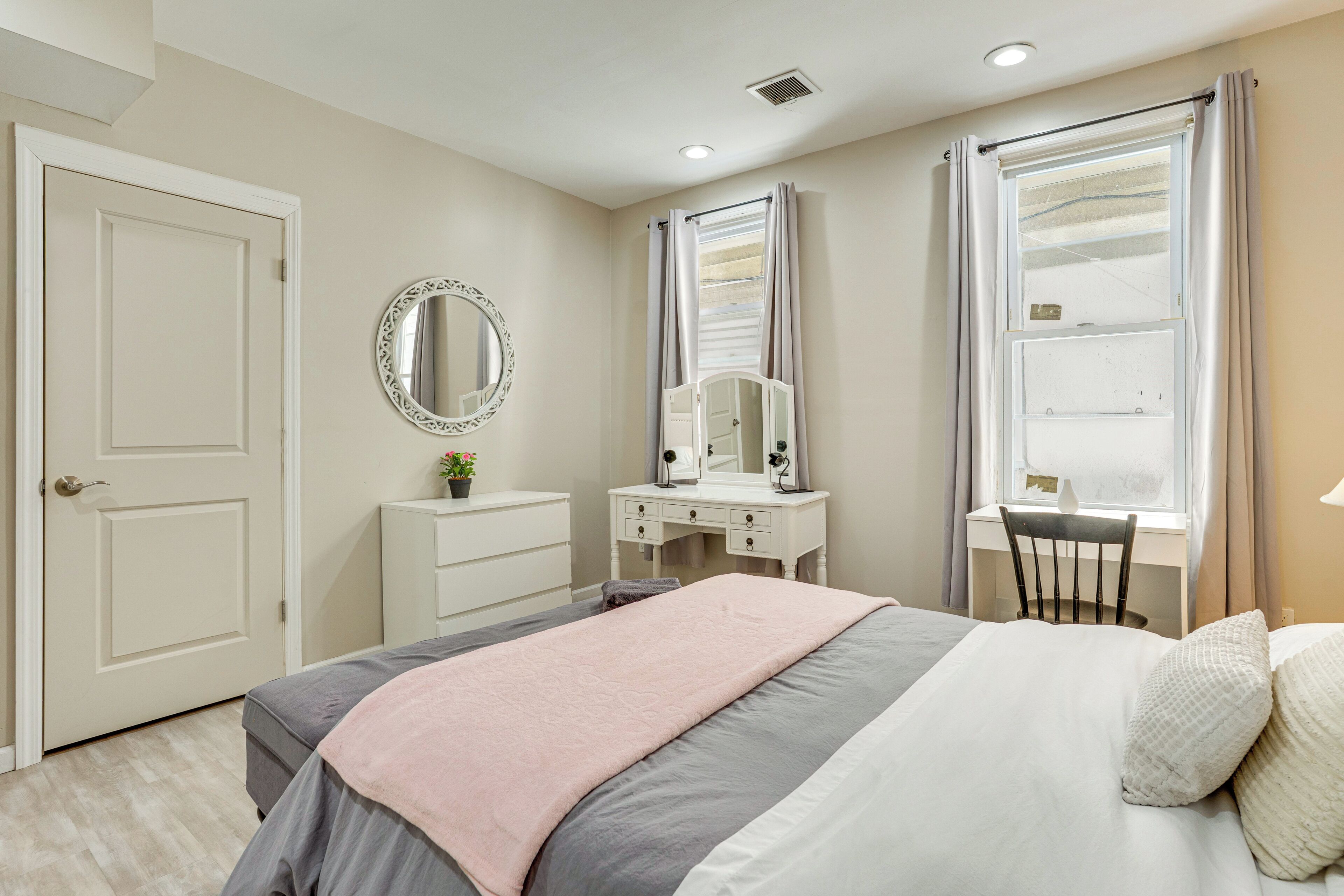 Um quarto com cama, cômoda, penteadeira com espelho e janela com cortinas.