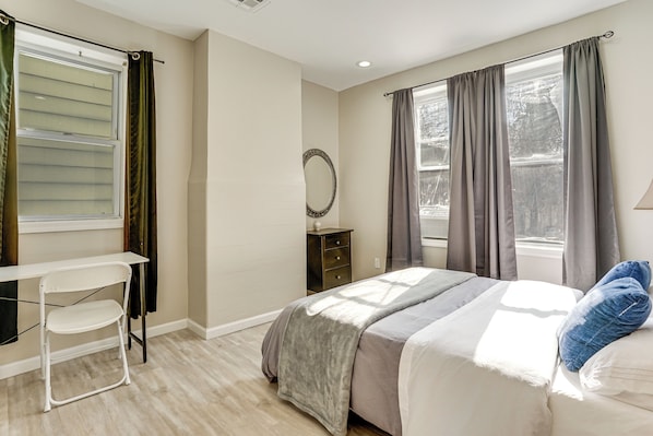 Un dormitorio con cama, escritorio, silla, cómoda y ventana con cortinas.