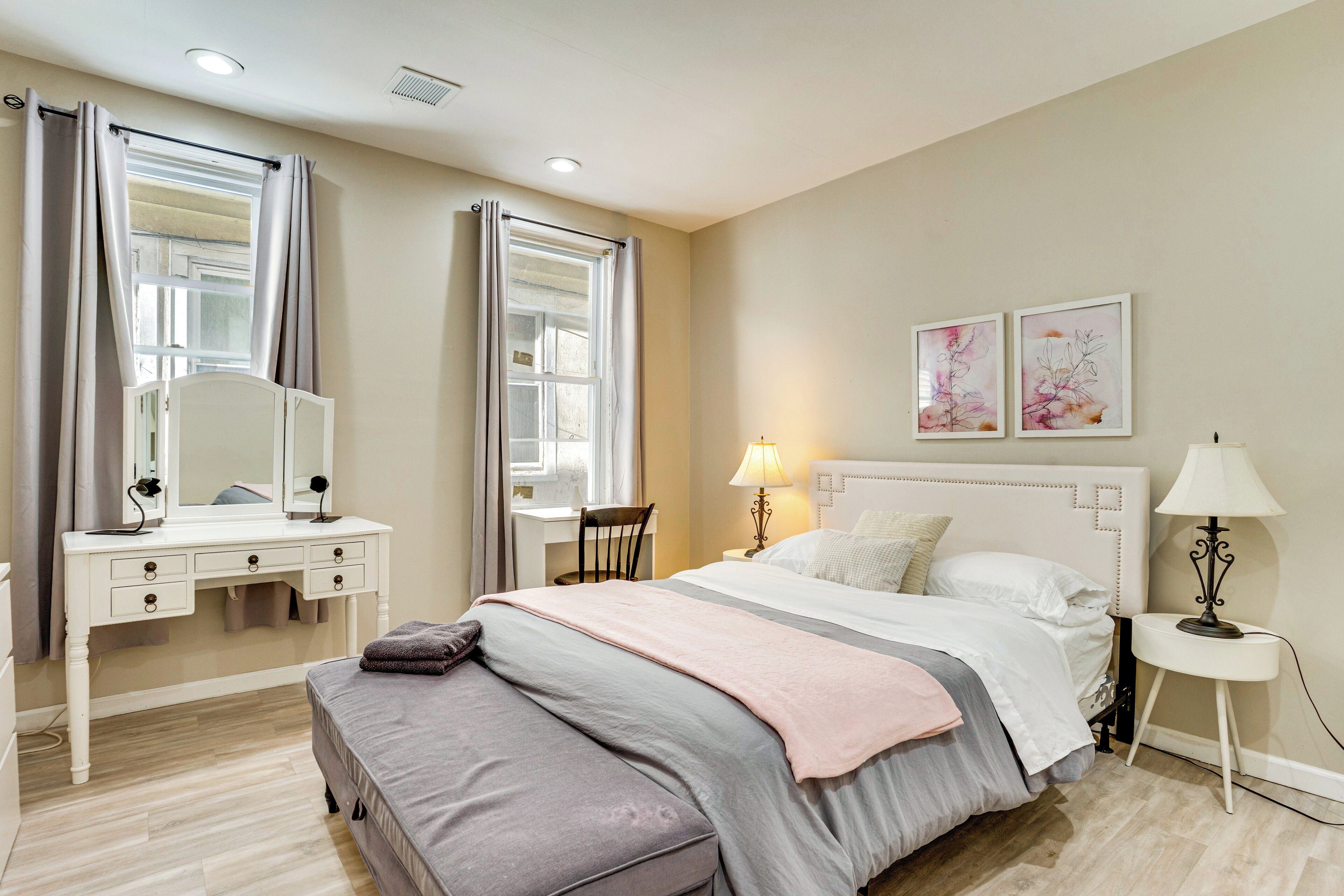 Una camera da letto con un letto, una scrivania, una sedia, un comodino con una lampada e due opere d'arte incorniciate appese al muro.