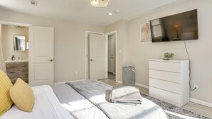 A bedroom with a bed, a TV mounted on the wall, a dresser, and a trash can. - Updated Duplex - 3 Mi to Newark Penn Station! (Newark)