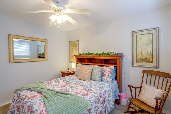 A bedroom with a bed, a chair, a nightstand, a mirror, and a ceiling fan.