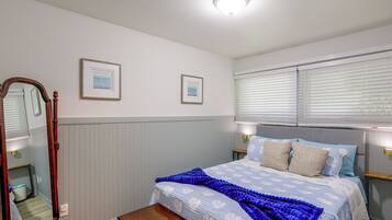 Una camera da letto con un letto, uno specchio, due quadri incorniciati, una finestra con persiane e un comodino.