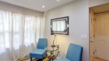 A room with two blue chairs, a small glass table with a lamp, a mirror on the wall, and a door.