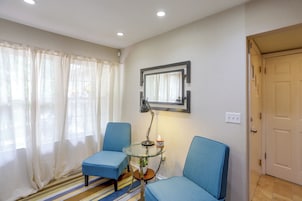 Una habitación con dos sillas azules, una pequeña mesa de vidrio con una lámpara, un espejo en la pared y una puerta.