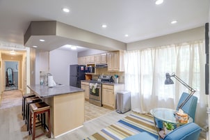 Una cocina moderna con una isla central, electrodomésticos de acero inoxidable y un comedor con mesa de vidrio y sillas azules.