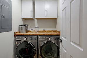 A laundry room with two front-loading washers and dryers, wooden cabinets above, and a metal door to the left. - Stone Manor-luxury Catawba Island Home w/ Hot Tub (Port Clinton)