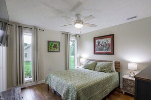 A bedroom with a bed, two bedside tables, a ceiling fan, and two windows with curtains. - Stone Manor-luxury Catawba Island Home w/ Hot Tub (Port Clinton)