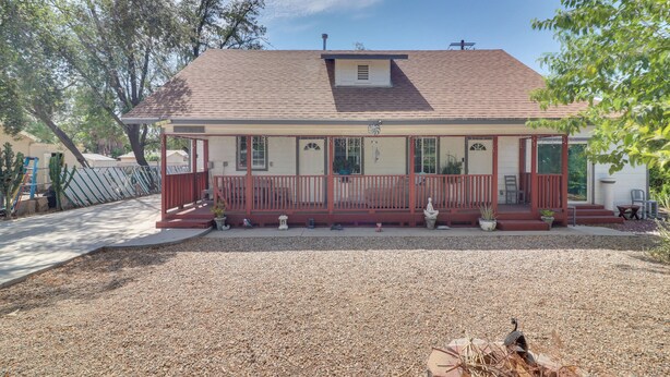 A single-story house with a front porch, a small attached garage, and a gravel driveway. - Sunny Hemet Escape w/ Covered Porch & Fire Pit (Hemet)