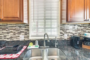 Una cocina con un lavamanos doble, armarios de madera, una ventana con persianas y un salpicadero con diseño de mosaico.